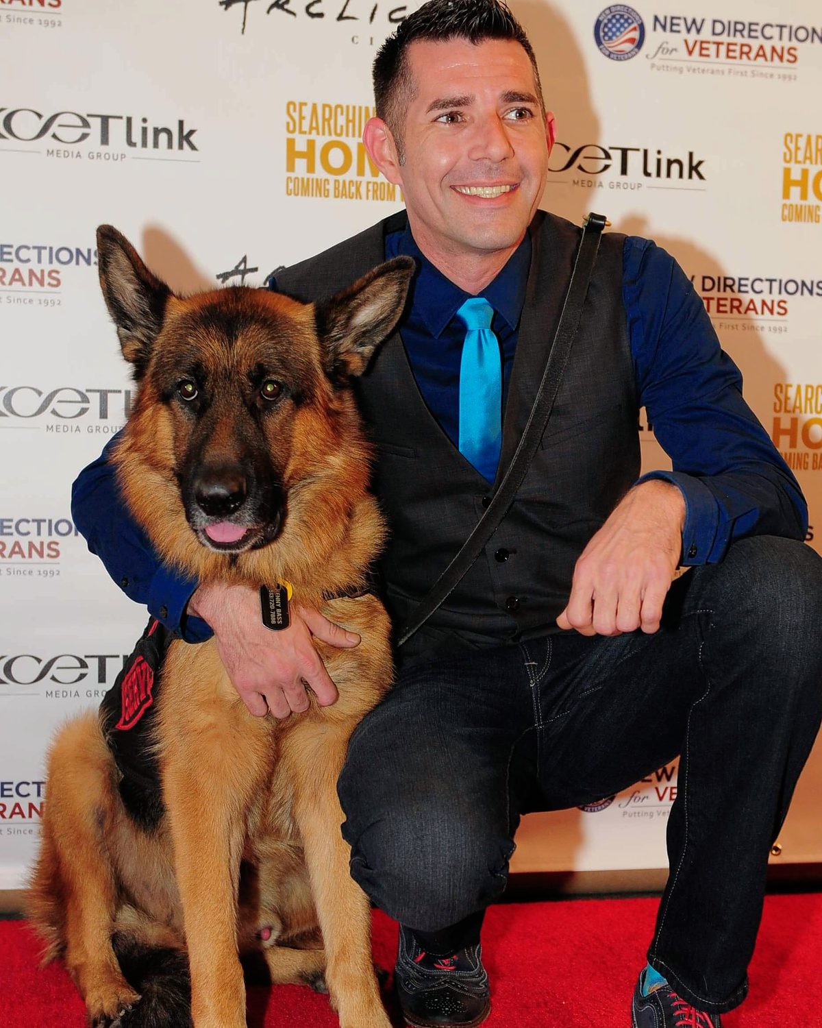 Kenny Bass with Atlas, his German Shepherd service dog, on a red carpet at a media event.