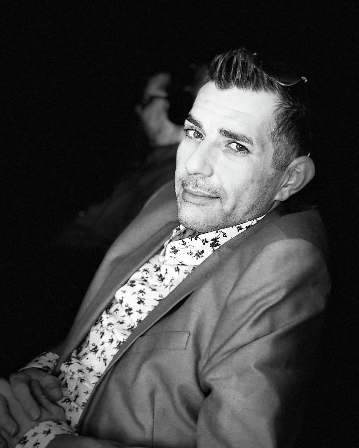 Black-and-white editorial portrait of Kenny Bass seated in a suit and patterned shirt.